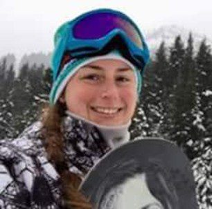 Young woman smiling in winter gear with snowboard in snowy forest.