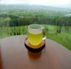 A glass of green tea on a table overlooking a lush green landscape.
