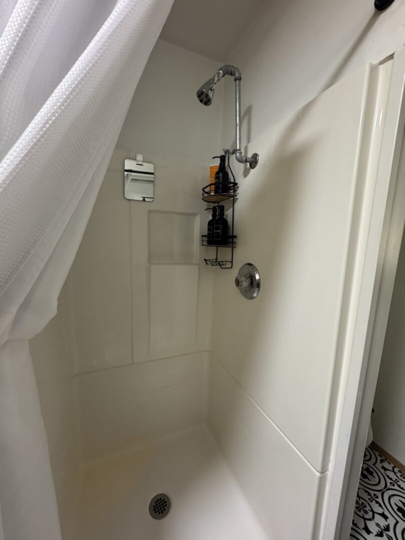 A clean white shower stall with toiletries and a curtain.