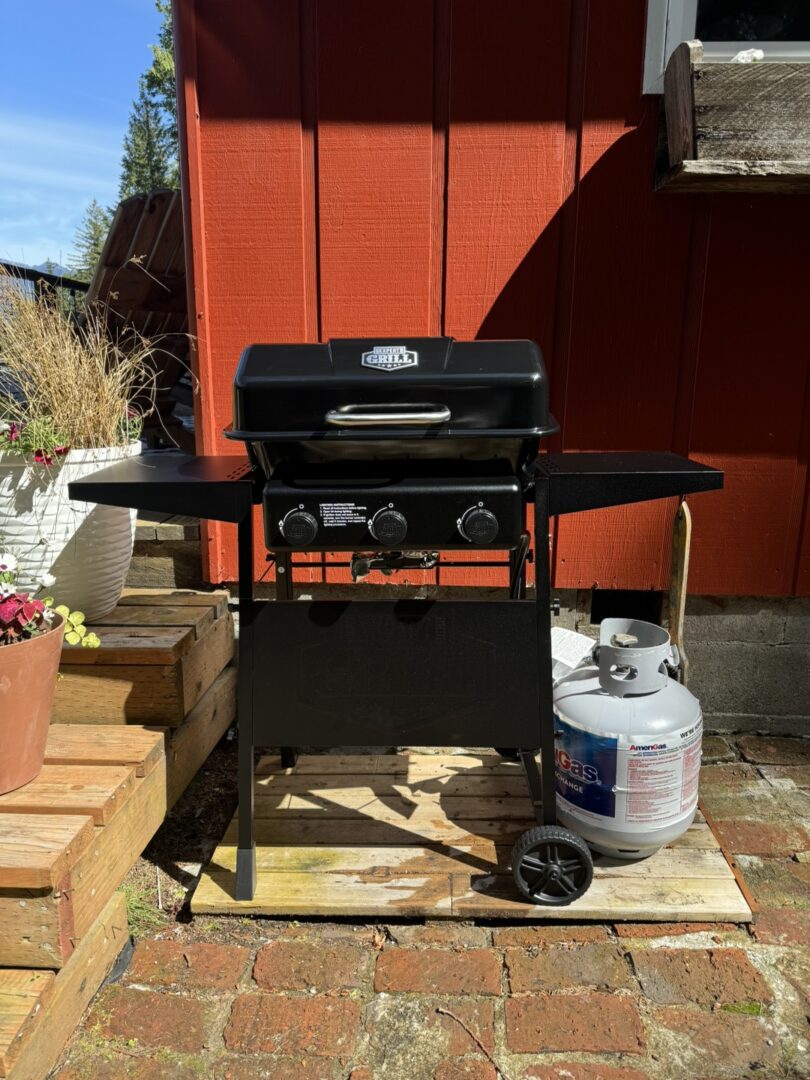 A black propane grill with side tables on a patio.