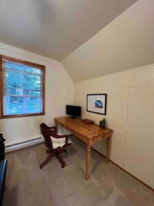 Cozy wooden desk setup with a chair, lamp, and monitor in a small room.