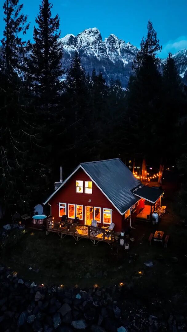Cozy cabin warmly lit at night surrounded by dark forest.