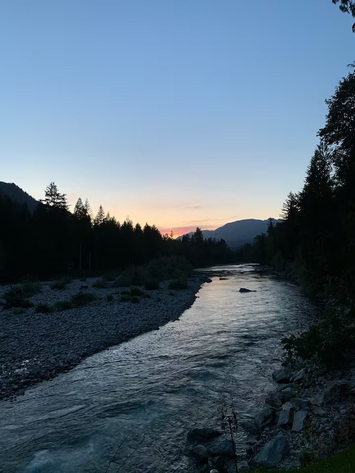 A serene river flowing through a forested valley at sunset.
