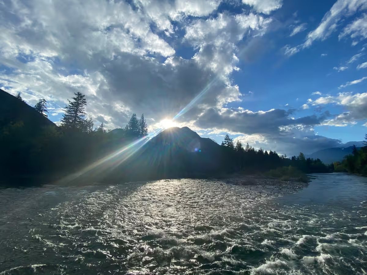 Sunlight breaks through dramatic clouds over a rippling lake surrounded by trees.