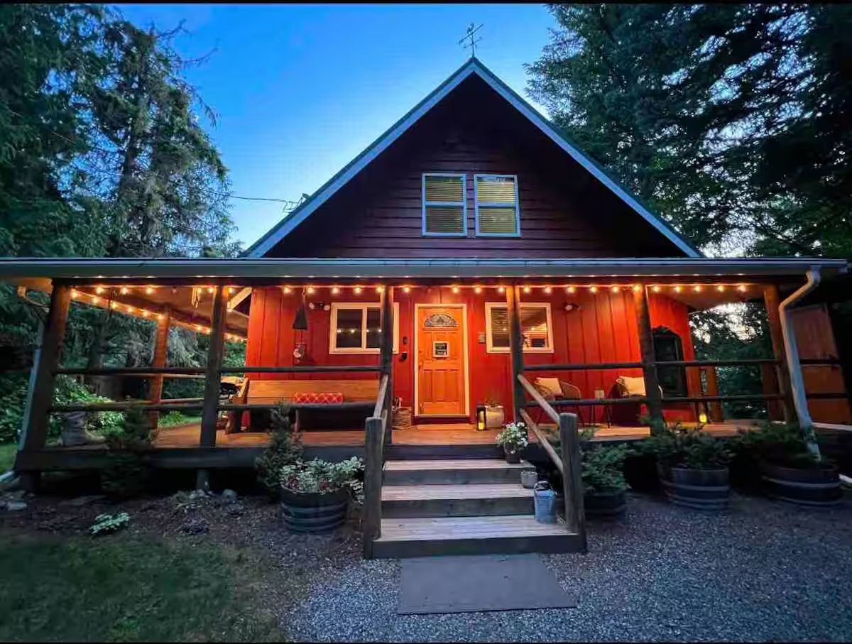 Cozy wooden cabin lit warmly at dusk with string lights.