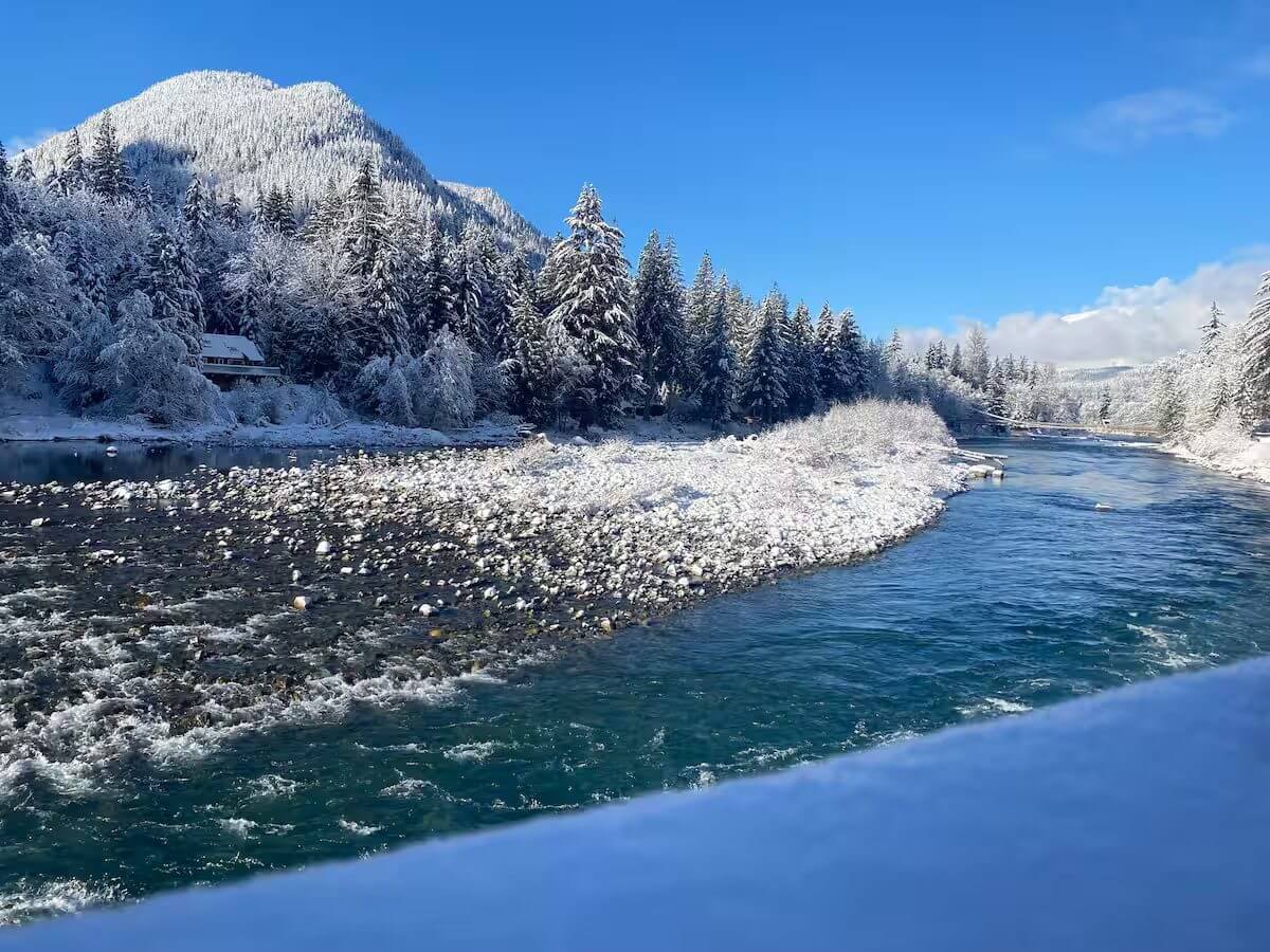 Snowy landscape with a partially frozen river under a clear blue sky.