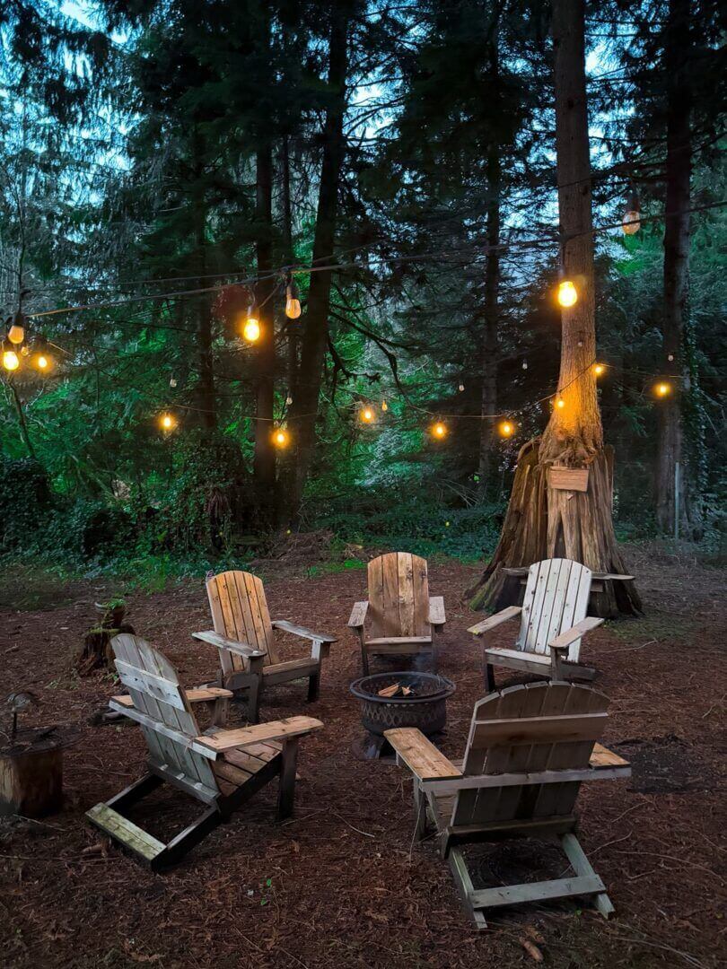 Cozy outdoor seating with hanging lights in a forest setting at dusk.