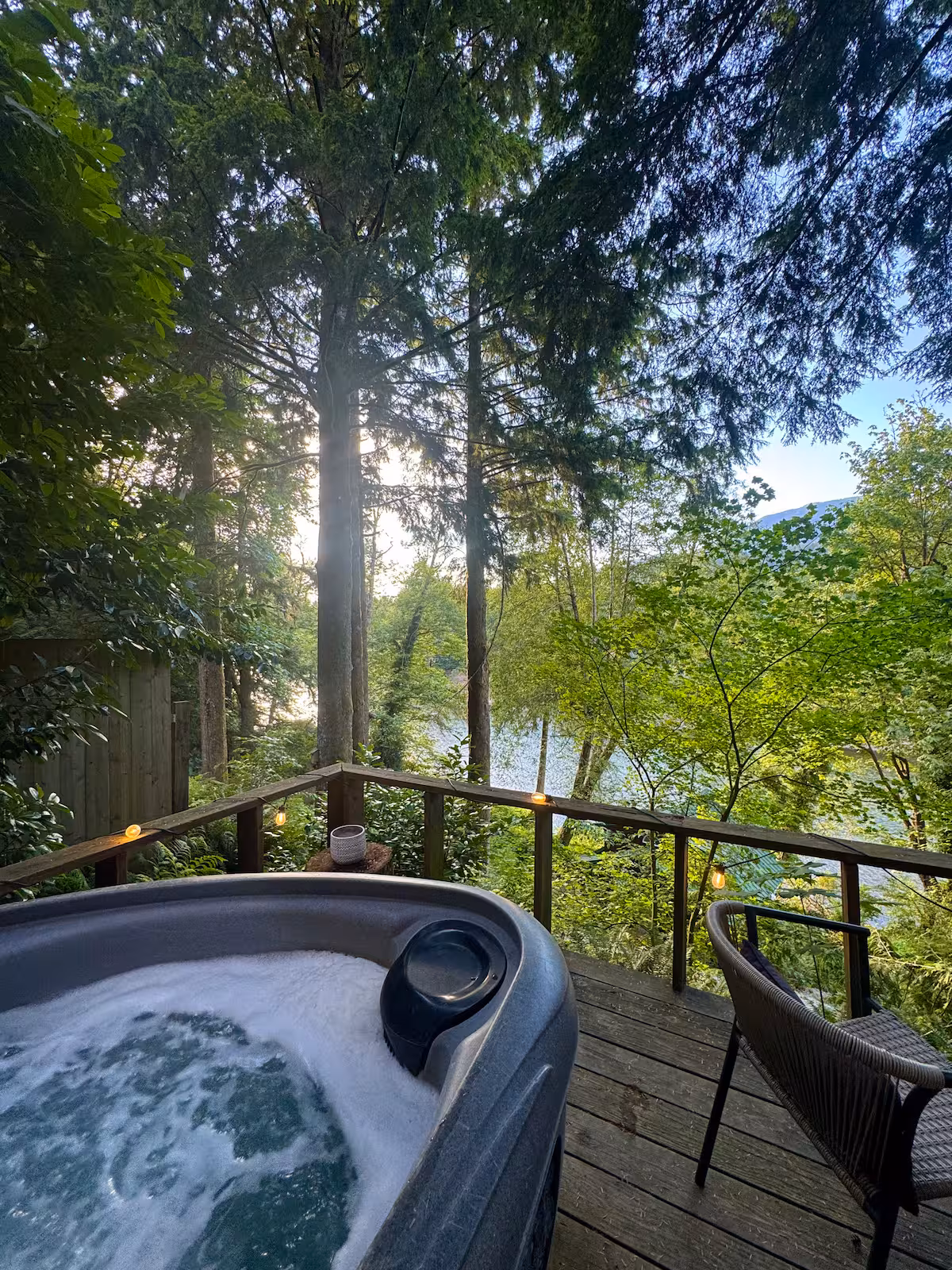 Sunlight filters through trees onto a cozy outdoor hot tub area.