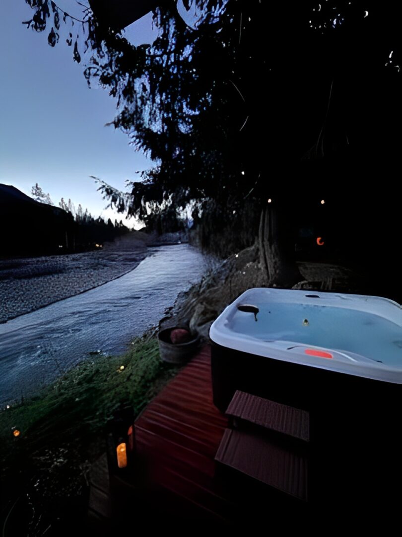 A hot tub beside a river at dusk with trees and hills in the background.