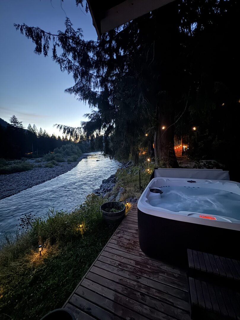 A hot tub beside a river at dusk with cozy lighting.