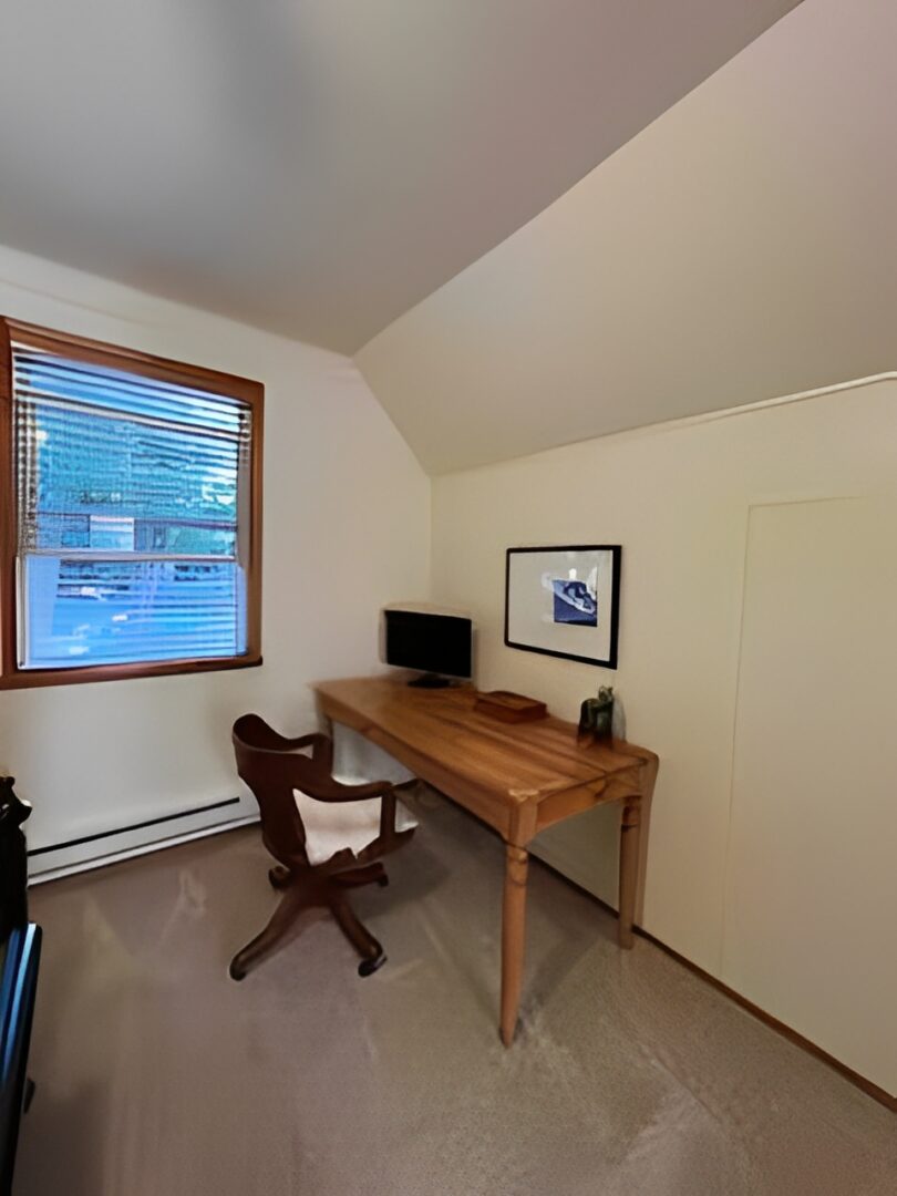 A small home office with a wooden desk and chair under a window.