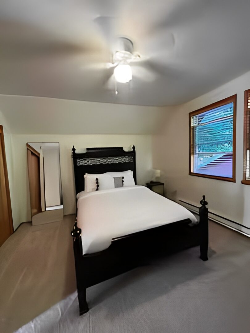 Cozy bedroom with a black wooden bed and white linens under a ceiling fan.
