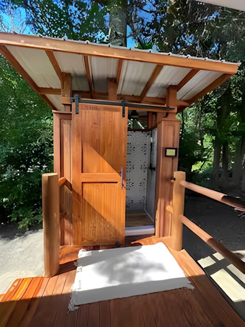 A wooden outdoor shower stall with a roof and privacy door.