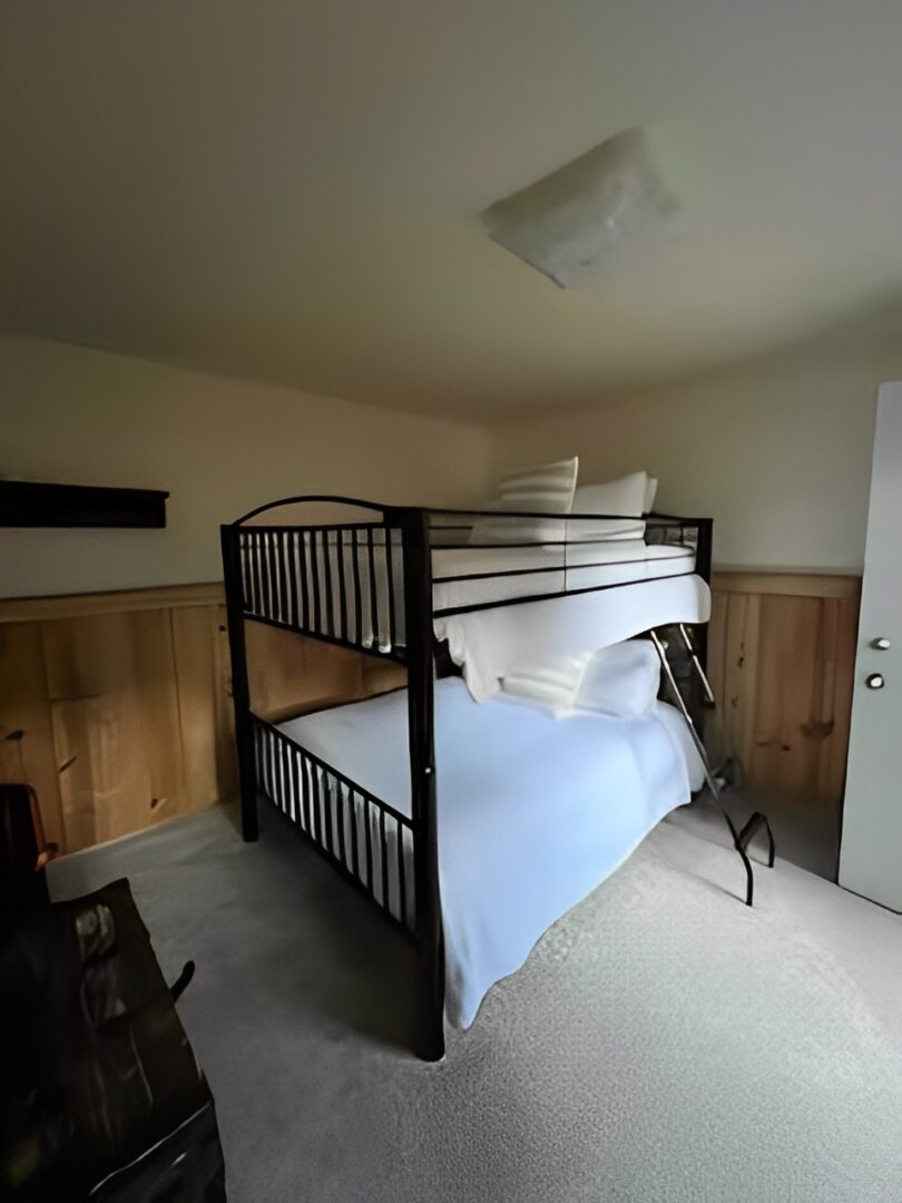 Bunk bed with black metal frame in a cozy room with wooden paneling.